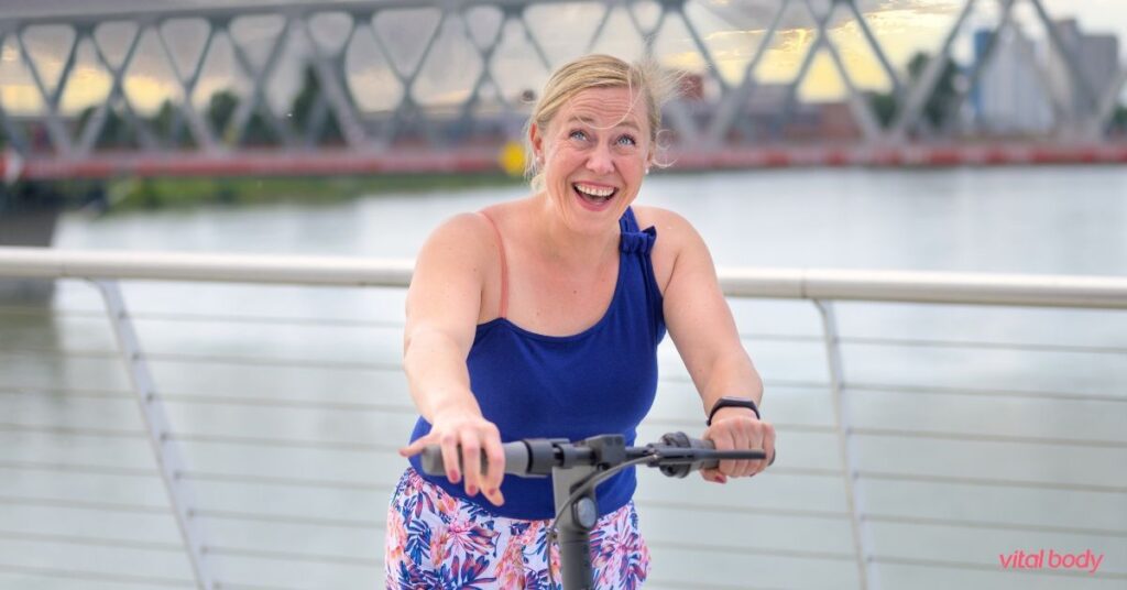 A smiling woman riding a scooter outdoors, feeling energetic and healthy while losing weight on a GLP-1 with nutrition coaching