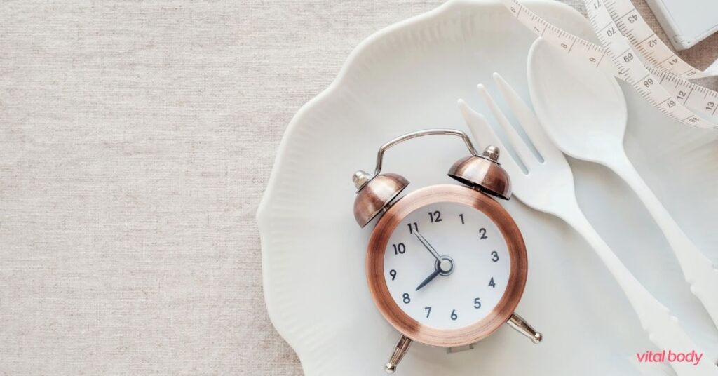 Alarm clock on an empty white plate with a fork, spoon and measuring tape