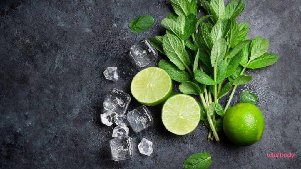 Fresh mint, halved limes and ice cubes on a dark stone surface