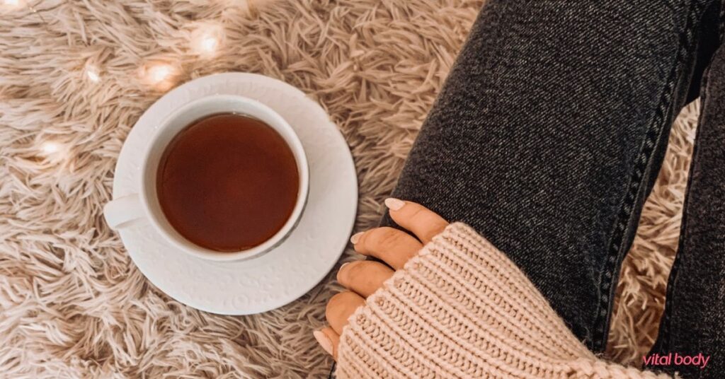 A cup of tea on a soft rug beside a woman in a cosy knit sweater, a quiet moment of self-care