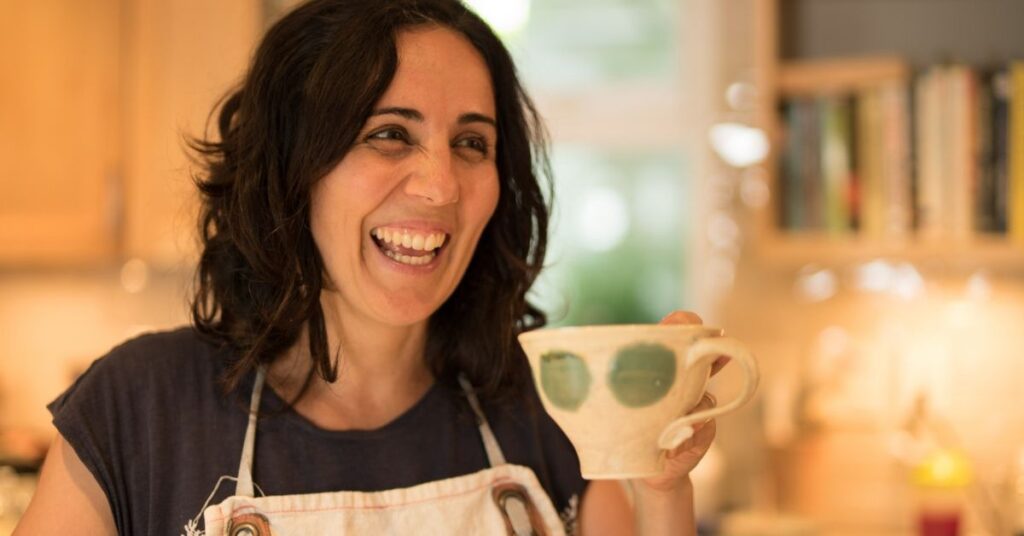 Zan Romeder, owner of Vital Body, laughing in her kitchen with a cup of tea